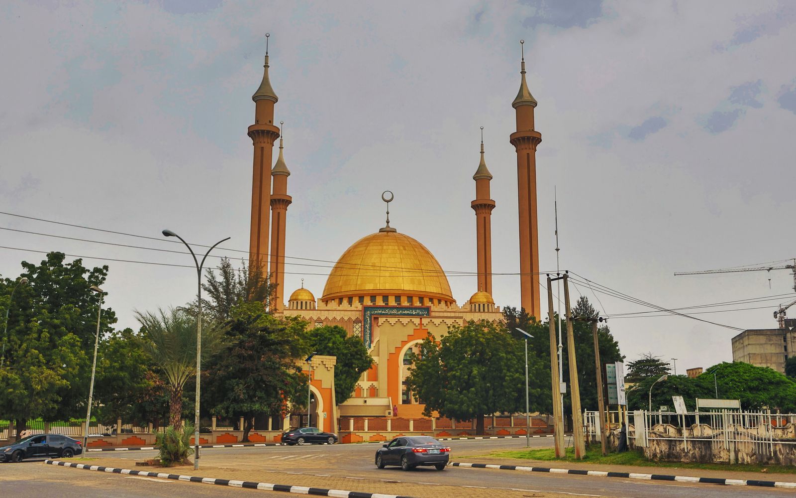 A majestic mosque with a golden dome and tall minarets photographed during the day in a city setting.